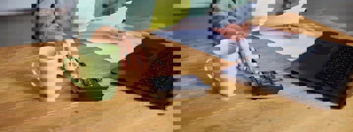 Picture of a hand tapping on a calculator with a laptop beside