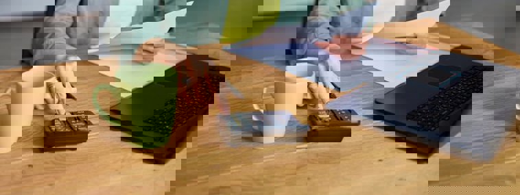 picture of a lady with a laptop, calculator holding paper